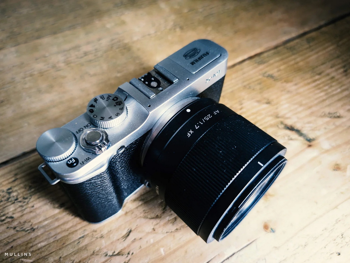 Компактний об'єктив Viltrox AF 25mm f/1.7 Air на сріблястій тушці Fujifilm X-M1 на дерев'яній поверхні